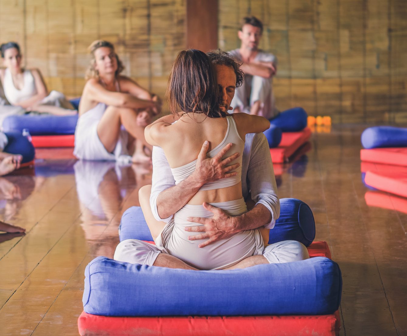 A couple embracing while seated on floor cushions in a group session room.